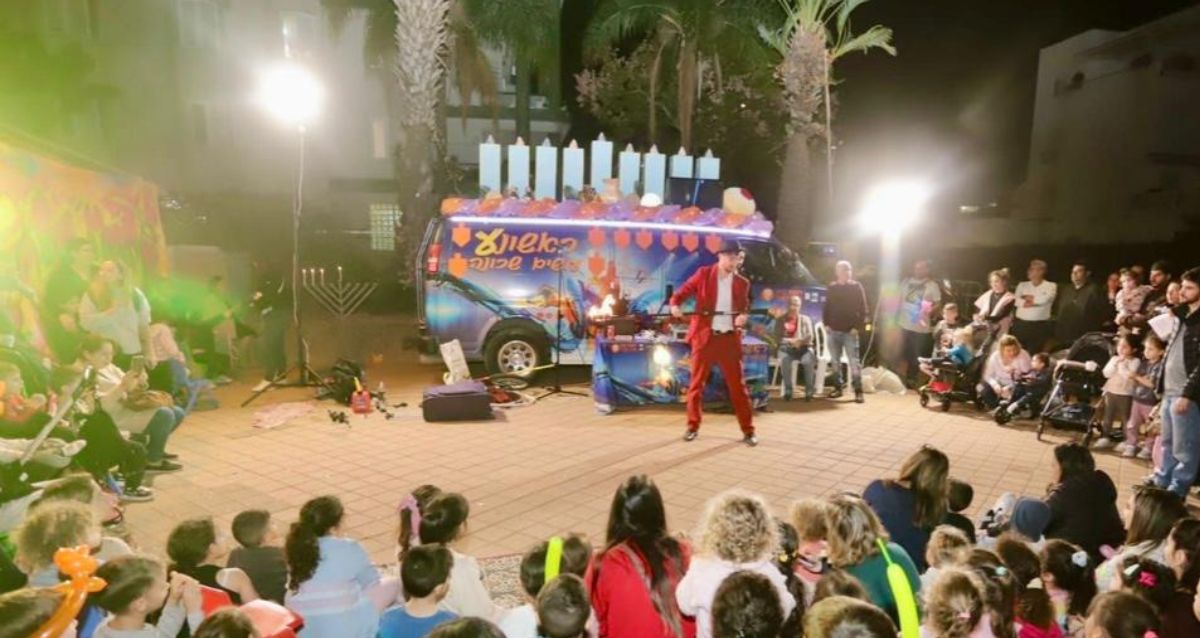 פעילות חנוכה למשחות וילדים, ילדים והורים צופים במופע של שחקן ומאחוריו חנוכיה ענקית, צילום: עיריית ראשון לציון