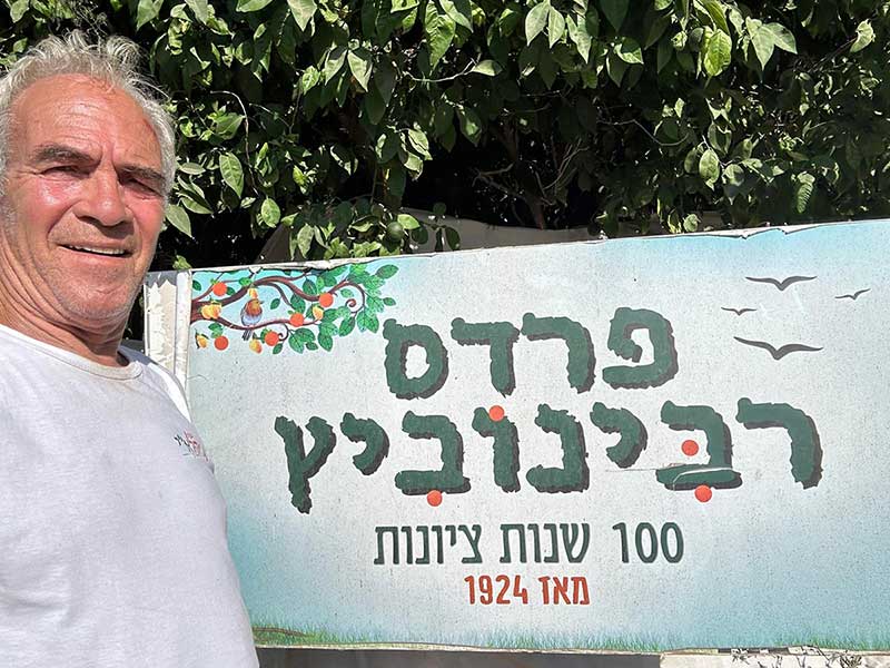 עו״ד שמואל רביב רבינוביץ על רקע שלט: פרדס רבינוביץ. 100 שנות ציונות מאז 1924