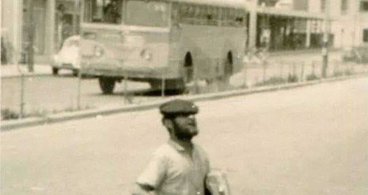 מוישה דודל האגדי. ברקע, תחנת אגד הישנה ותחנת הדלק סונול. מוישה צועד בכביש, חובש כובע קסקט