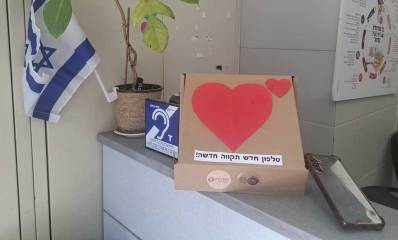 תתרמו מכל הלב. על ארונית טלפון משומש וקרטון עם תמונות של לב וכיתוב: טלפון חדש תקווה חדשה!
