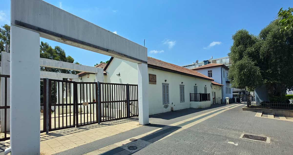 בית שליט. בניין חד קומתי עם גג רעפים. משמאל שער כניסה ממתכת רחב מאוד ושני עמודים מבטון בצידי הכניסה ומעליהם קורה של בטון.